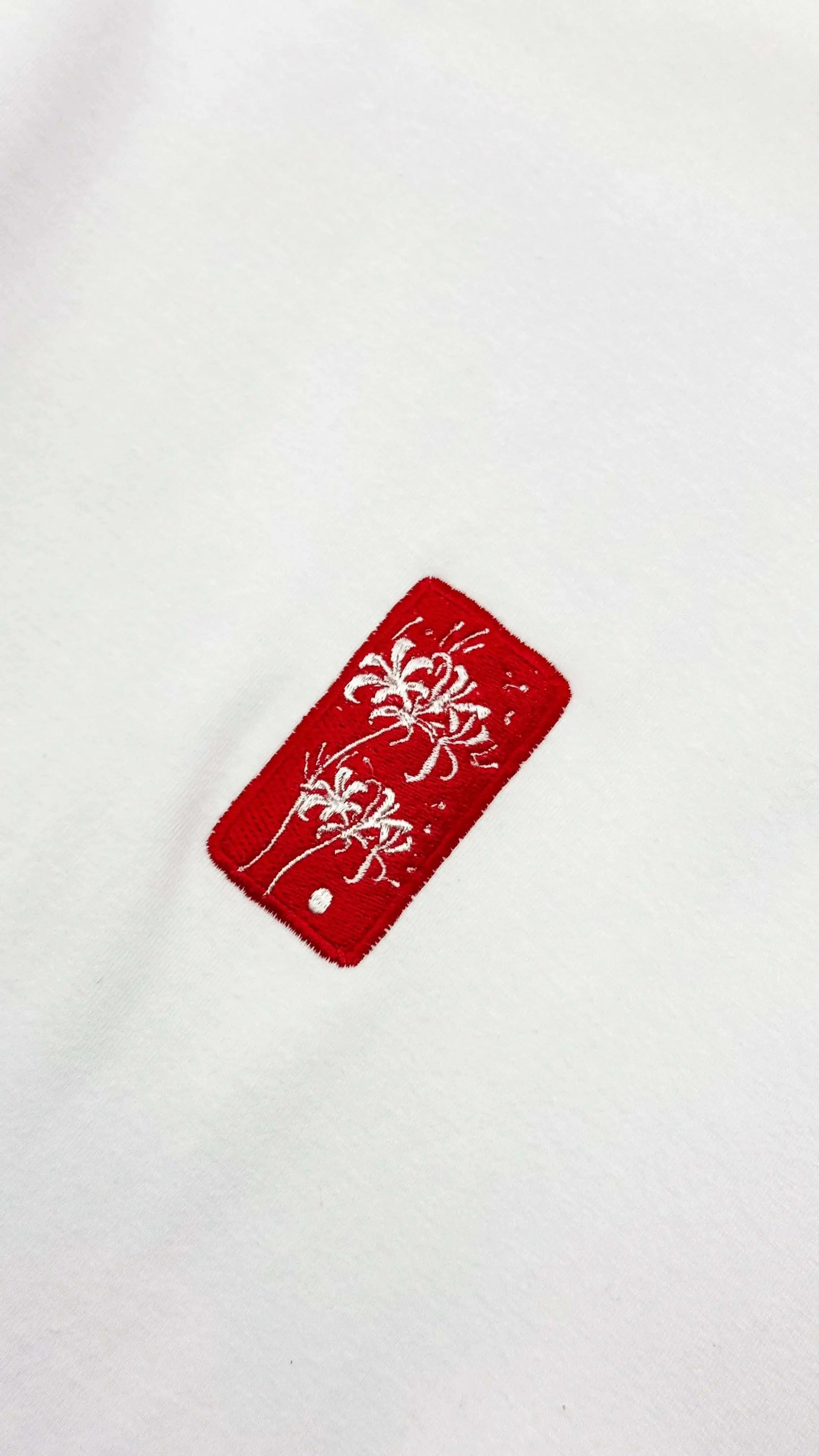Spider Lily – Weißes, kurz geschnittenes Oversized-T-Shirt mit rotem, gesticktem Logodetail auf weißem Stoff.