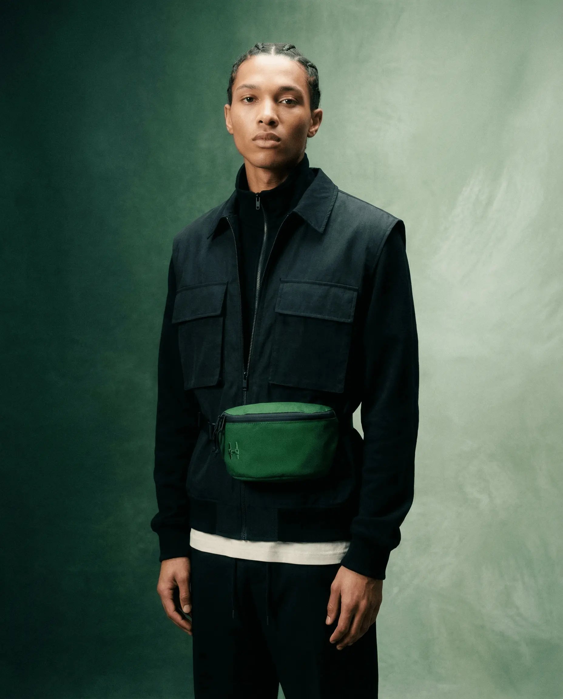 Model wearing Sora 2.0 - Forest Green fanny pack with a stylish black outfit against a textured background.